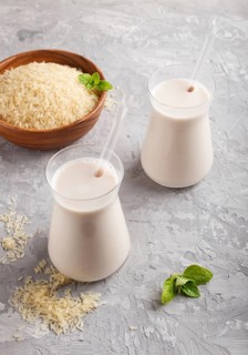 Organic non dairy rice milk in glass and wooden plate with rice seeds on a gray concrete background