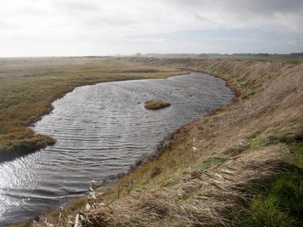 Marshland behind vegetated shingle with lagoon water bounded by costal defence sea wall, Alderton,