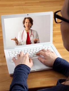 Symbolic image of telemedicine, patient speaking to a doctor in a video conference from home