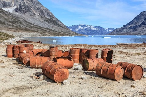Rusted oil barrels on a fjord in front of steep mountains, remains of a US airbase from the Second