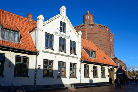 A white traditional building with a tiled roof in the foreground in front of an unusual round tower
