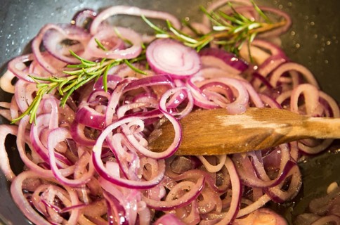 Close up onion rings cooking in wok pan with rosemary wooden stirrer