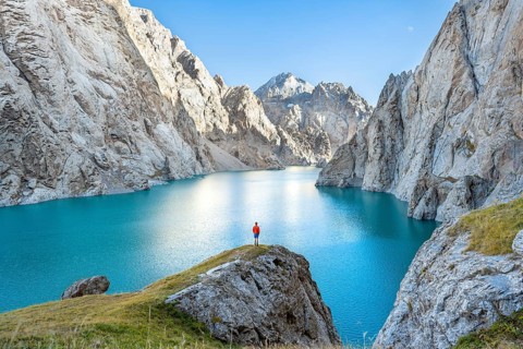 Young man at the turquoise mountain lake Kol Suu with rocky steep mountains, Kol Suu Lake, Sary