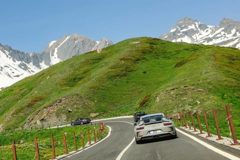 Three Porsche sports cars driving on a mountain road above the tree line through the French Alps,