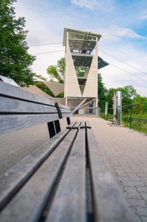 A long wooden bench runs along a hiking trail with a view of a modern observation tower,