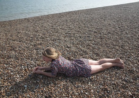 Model released young teenage girl wearing floral dress lies on shingle beach near the sea