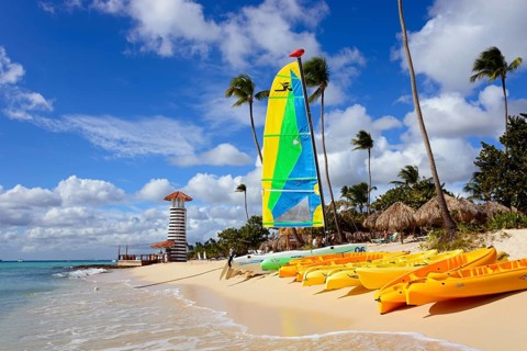 Colourful sailboat on tropical beach with lighthouse and kayaks in the sand, lighthouse, bar of