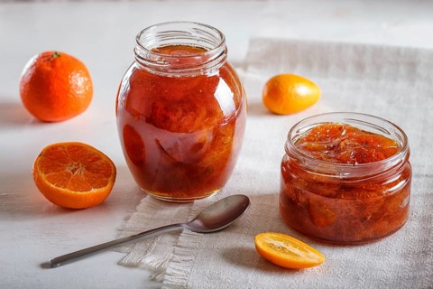 Tangerine and kumquat jam in a glass jar with fresh fruits on white background. Homemade, close up