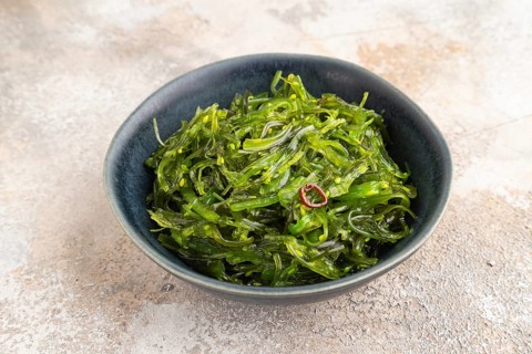 Chuka seaweed salad in blue ceramic bowl on brown concrete background. Side view, close up