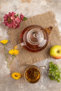 Red tea with herbs in glass teapot on brown concrete background and linen textile. Healthy drink