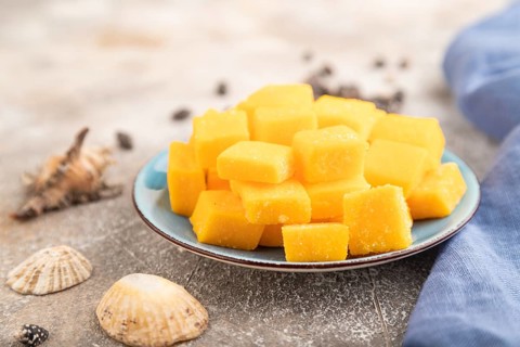 Dried and candied mango cubes on blue plate on brown concrete background and linen textile. Side