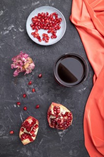 Glass of pomegranate juice on a black concrete background with red textile. Top view, close up,