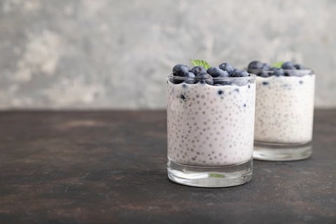 Yogurt with blueberry and chia in glass on black concrete background. Side view, close up, copy