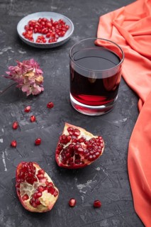 Glass of pomegranate juice on a black concrete background with red textile. Side view, close up