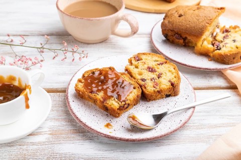Homemade cake with raisins, almonds, soft caramel and a cup of coffee on a white wooden background