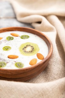 Yogurt with kiwi, gooseberry, chia and almonds in wooden bowl on gray wooden background and linen