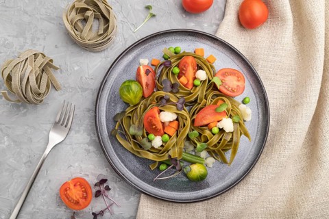 Tagliatelle green spinach pasta with tomato, pea and microgreen sprouts on a gray concrete