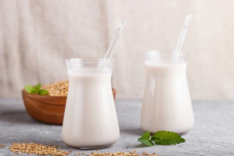 Organic non dairy oats milk in glass and wooden plate with oats seeds on a gray concrete background
