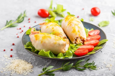 Stuffed baked squid with greens on a blue ceramic plate on a gray concrete background, side view,