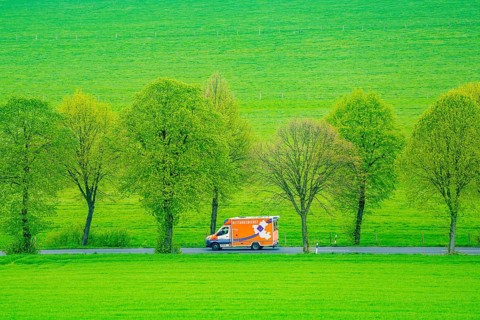 Ambulance on a country road, green fields, meadows, trees line the 2-lane road, spring, near