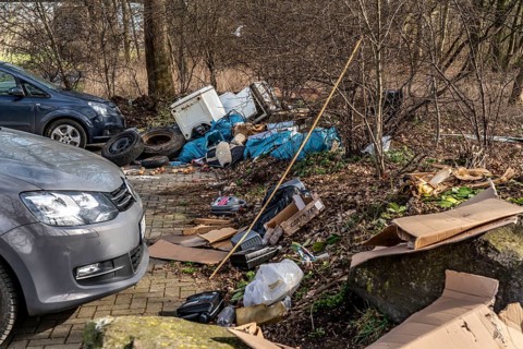 Illegal waste disposal in a car park, in a wooded area, tyres, furniture, refrigerators, household