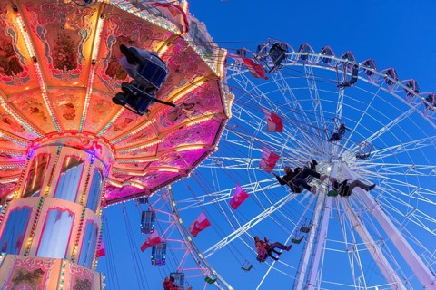 Illuminated chain carousel and Ferris wheel at night with cheerful people, funfair, wave flight,