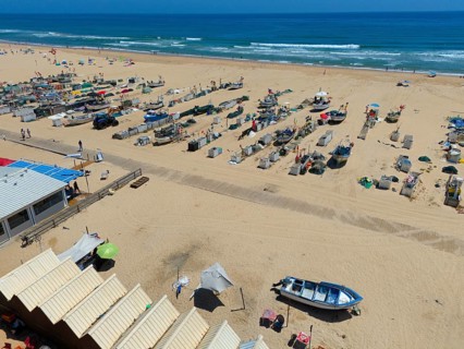 Beach with many boats, huts and parasols. In the background the sea and some beach visitors, aerial