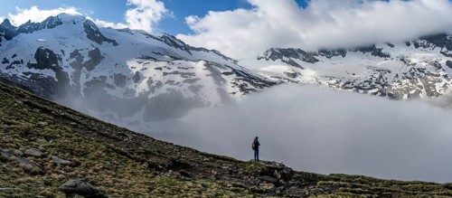 Mountaineer on a rock in front of a mountain landscape, high fog in the valley, panorama with