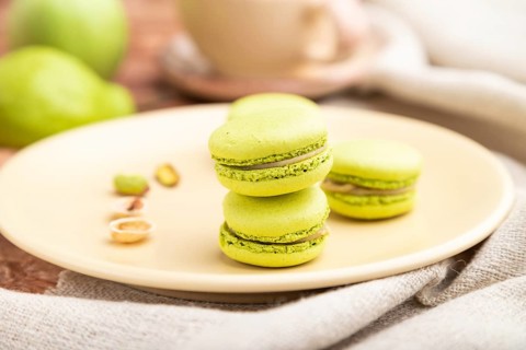 Green macarons or macaroons cakes with cup of coffee on a brown concrete background and linen