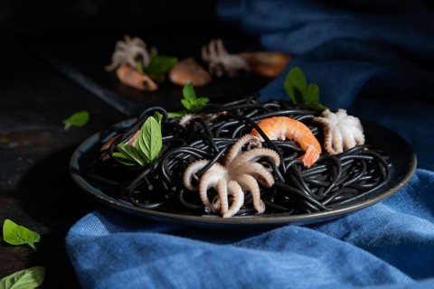 Black cuttlefish ink pasta with shrimps or prawns and small octopuses on black concrete background