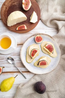 Summer appetizer with pear, cottage cheese, figs and honey on a white wooden background and linen