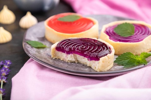 Sweet tartlets with jelly and milk cream with cup of coffee on a black concrete background and pink