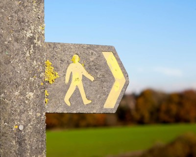 Close up of footpath sign with yellow human figure walking and direction arrow pointing the way,