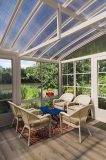 Beige wicker armchairs and blue wooden table in sunroom at back of luxurious residential home,