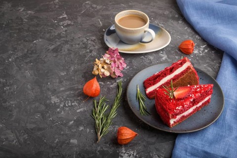 Homemade red velvet cake with milk cream and strawberry with cup of coffee on a black concrete