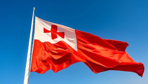 The flag of Tonga, Pacific island state, flutters in the wind, isolated against a blue sky