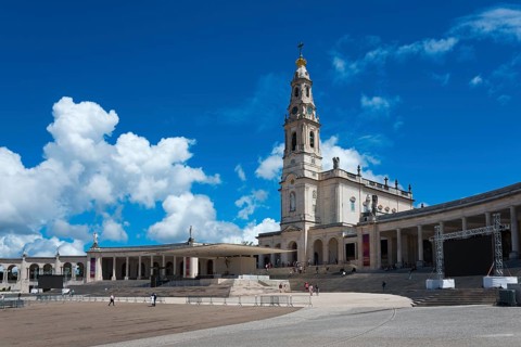 Spacious square with an imposing bell tower and surrounding colonnades under a blue sky, Basilica