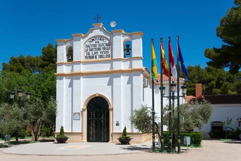 Historische Kapelle mit verschiedenen Fahnen und Bäumen unter blauem Himmel, Ermita y museo Virgen