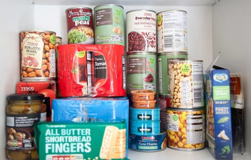 Tinned food piled up in domestic household kitchen cupboard including products from Tesco