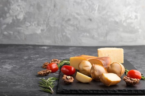Smoked cheese and various types of cheese with rosemary and tomatoes on black slate board on a