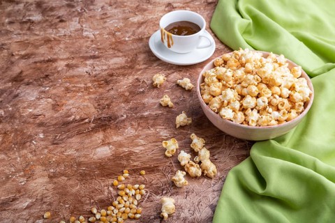 Popcorn with caramel in ceramic bowl on brown concrete background and green textile. Side view,