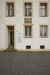 Facade of a historic building with white windows, door and a colourful family coat of arms in the