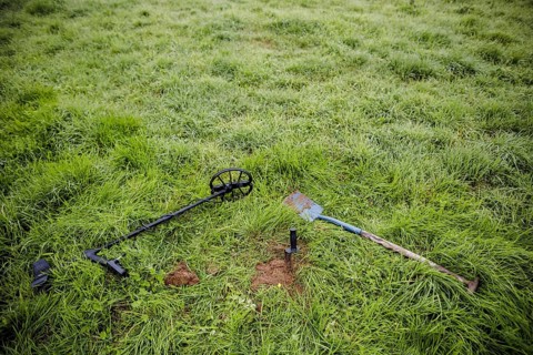 Symbolic photo on the subject of treasure hunting. A metal detector and a spade lie in a meadow.