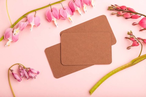 Brown business card with pink dicentra, broken heart flowers on pink pastel background. top view,