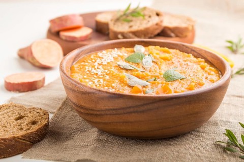 Sweet potato or batata cream soup with sesame seeds in a wooden bowl on a white wooden background