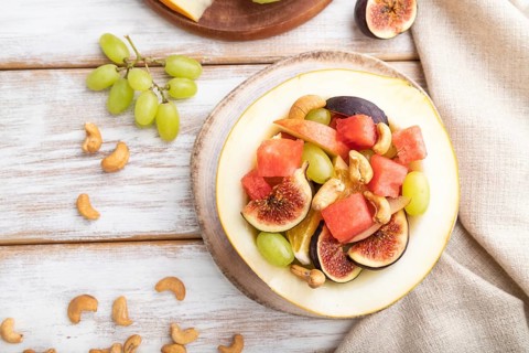 Vegetarian fruit salad of watermelon, grapes, figs, pear, orange, cashew on white wooden background
