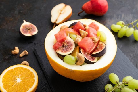 Vegetarian fruit salad of watermelon, grapes, figs, pear, orange, cashew on slate board on a black