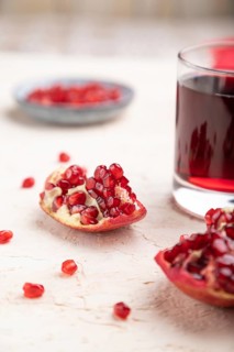 Glass of pomegranate juice on a white concrete background with red textile. Side view, close up,