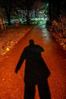 Pedestrian path through a park, in the evening, dark only little illumination by street lamps,