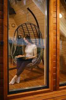 Young woman sitting in a cozy hanging chair, engrossed in reading a book. A woman spends her